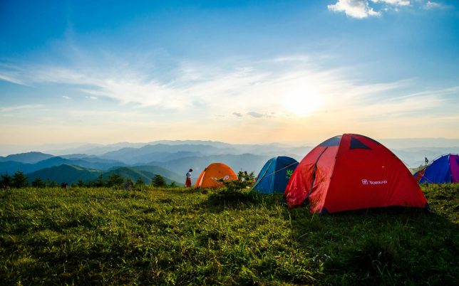 Vibrant tents on a grassy mountain ridge with a stunning sunrise view, ideal for adventure.